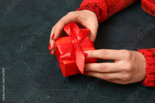 Fototapeta Naklejka Na Ścianę i Meble -  Female hands with red manicure and Christmas gift box on black grunge background