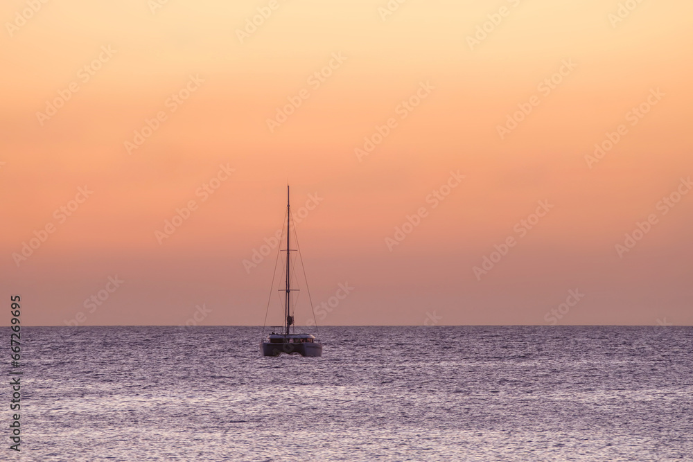 Sailboat on the ocean near the beach at sunset.