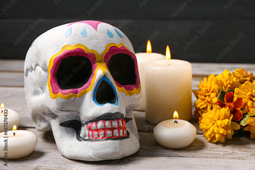 Painted skull with marigold flowers and candles on grey wooden table near black wall. Celebration of Mexico's Day of the Dead (El Dia de Muertos) Painted skull with marigold flowers and candles on grey wooden table near black wall. Celebration of Mexico's Day of the Dead (El Dia de Muertos)