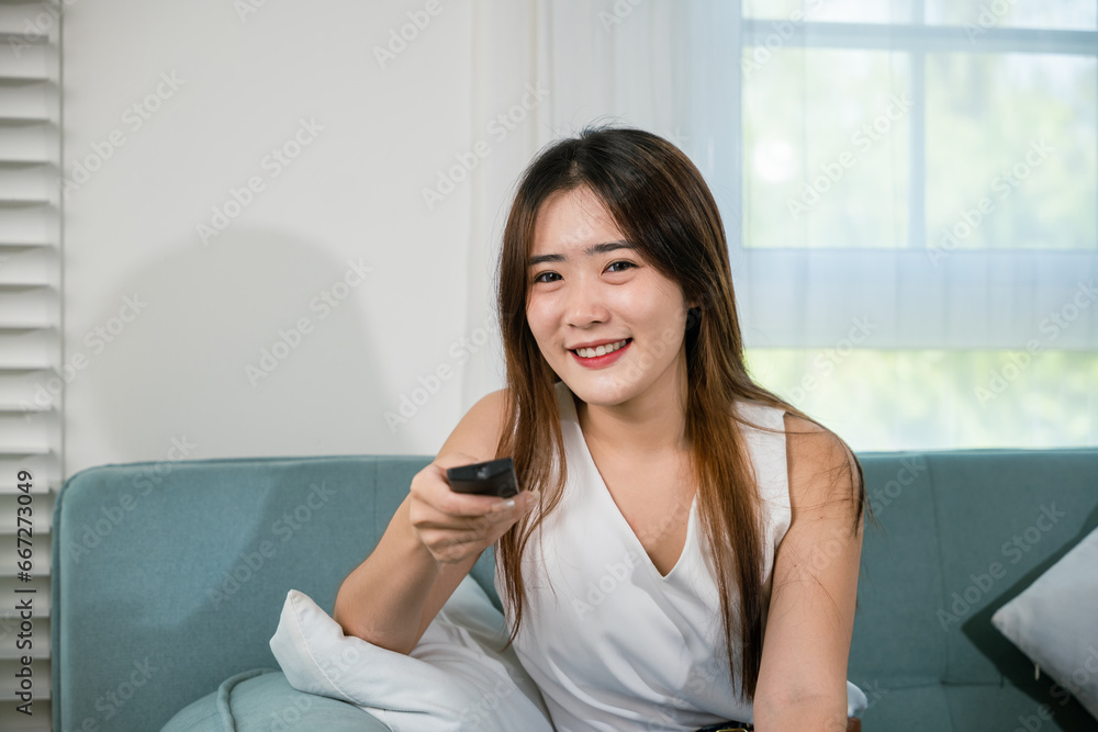 Happy female fun comedy video holding remote watching television, Asian young woman smiling sitting relaxing watch TV holding remote control on sofa in living room, Activity lifestyles concept Happy female fun comedy video holding remote watching television, Asian young woman smiling sitting relaxing watch TV holding remote control on sofa in living room, Activity lifestyles concept