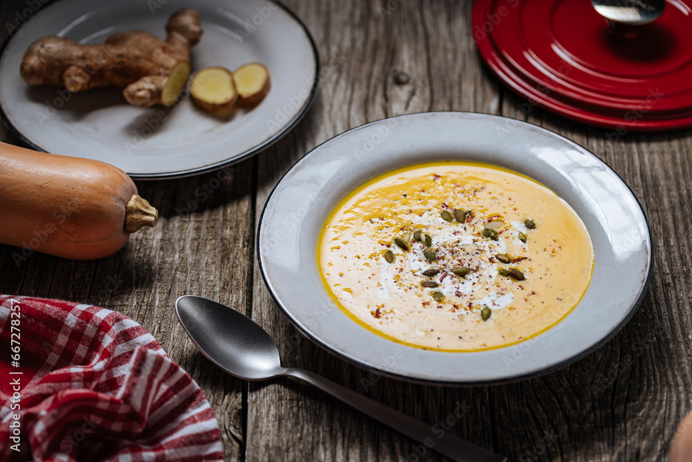 Creamy pumpkin soup garnished with cooking sauce served in white bowl on rustic wooden background. Seasonal warm food. Autumn Appetiser Creamy pumpkin soup garnished with cooking sauce served in white bowl on rustic wooden background. Seasonal warm food. Autumn Appetiser