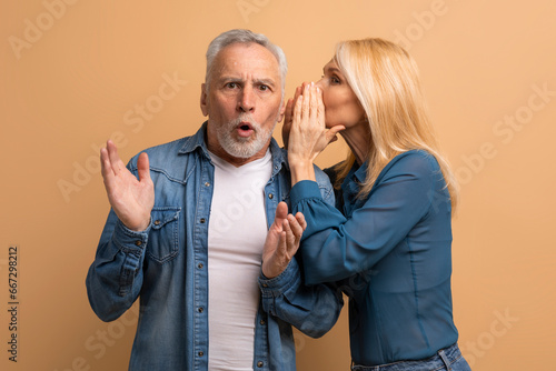Mature woman sharing secret with her husband, beige background photo