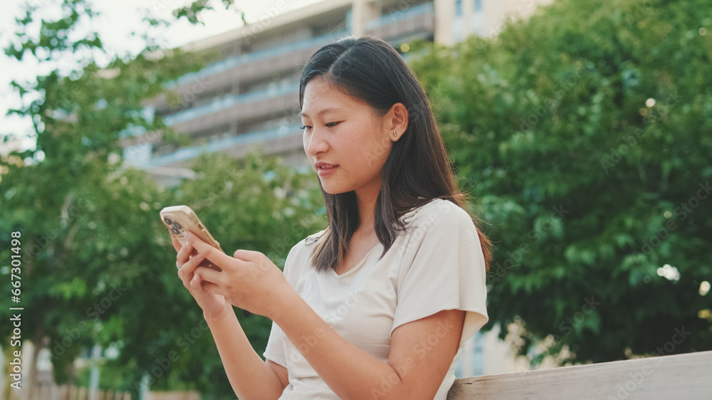 Close up, beautiful young woman sits on bench in city park using mobile phone, blurred background Close up, beautiful young woman sits on bench in city park using mobile phone, blurred background