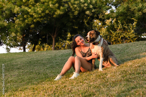 Young woman and her American Stanford dog relax on a hill during sunset sitting in the ark grass. photo