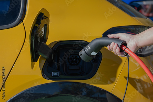 Anonymous person standing inserting charging power cable to electric vehicle at gas station photo