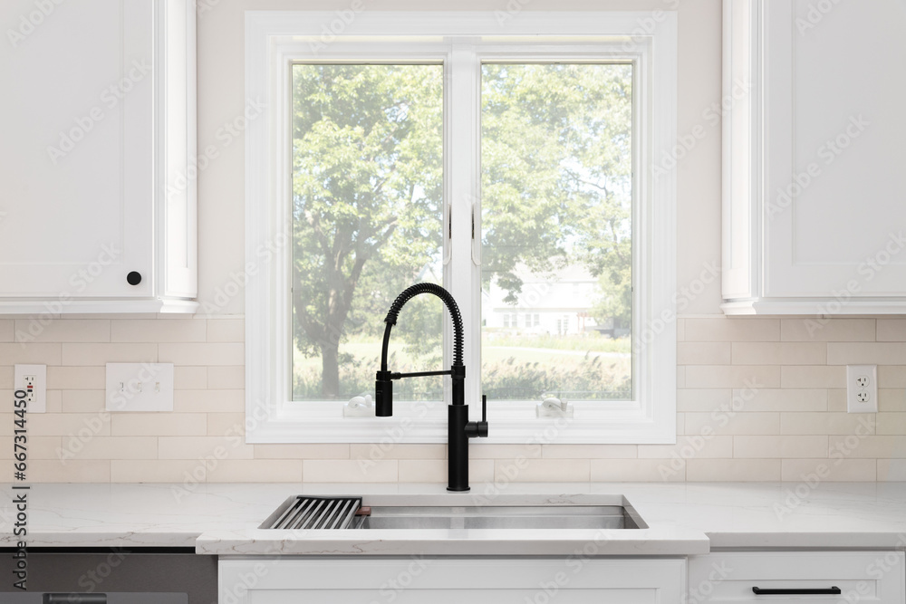A black faucet detail with white cabinets, brown subway tile backsplash, and white marble countertop. A black faucet detail with white cabinets, brown subway tile backsplash, and white marble countertop.