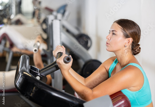 Young athletic woman training her arm muscles using machine in gym