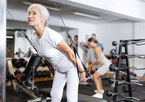 Mature woman working on a special machine with ropes to develop arm muscles
