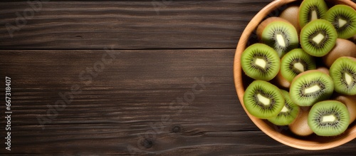 Kiwi fruits with slices in bowl on wooden table viewed from above