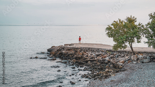 Boy standing on the stone dock (pier) and looking towards mediterranean sea, tree © 7