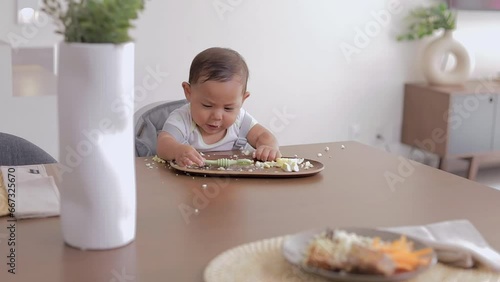 Baby led weaning concept. Baby eating with his hands sitting at the table, with a preloaded spoon photo
