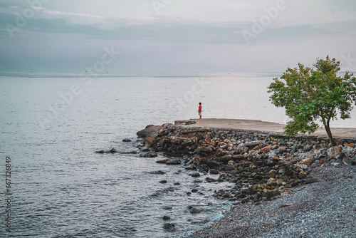 Boy standing on the stone dock (pier) and looking towards mediterranean sea, tree © 7