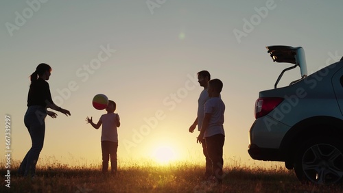 Family play, Travelling by car. Happy family travels by car. Parents, children stopped at campsite by car, Toy ball. Dad with child son, mother, children play with ball, next to car, beautiful sunset