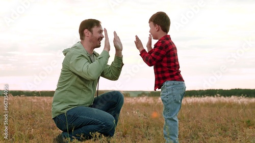 Positive boy gives high-five to father playing in middle of field in agricultural area