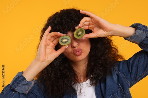 Woman covering eyes with halves of kiwi on yellow background