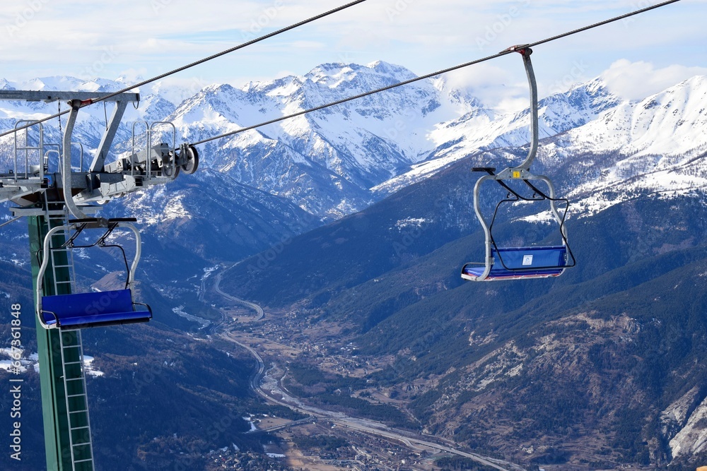 Empty chair lift for skiers and snowboarders overlooking Susa valley and Alpine village in Sauze D'Oulx ski resort, Piedmont, Turin, Northern Italy
