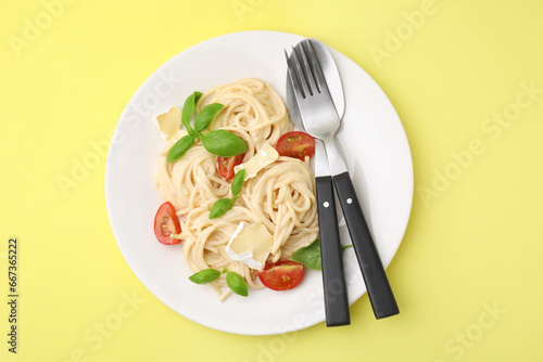 Delicious pasta with brie cheese, tomatoes, basil and cutlery on yellow background, top view