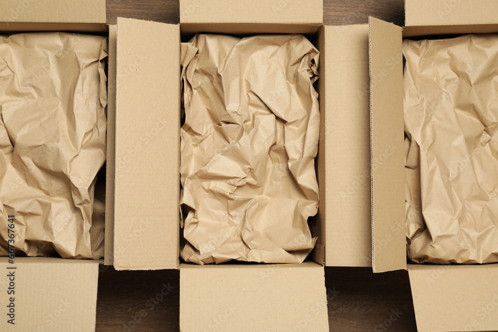 Open cardboard boxes with crumpled paper on wooden floor, flat lay. Packaging goods