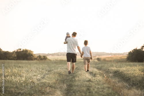 Having fun with kids, time for father and sons, family active weekend. Father and baby walking through the woods on a sunny summer day. Dad holds his son's hand and they are fooling around