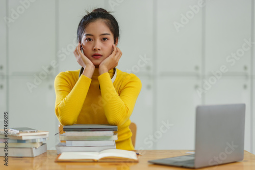 Confident Asian female student wearing wireless headphones studying online, searching for information, thinking analytically from documents, textbooks, laptop computer for business studies. photo