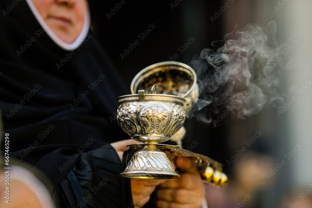 Obraz na płótnie Shallow depth of field (selective focus) details with the hand of a orthodox Christian nun holding a smoking metallic censer incense burner. w salonie