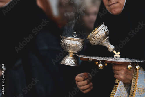 Shallow depth of field (selective focus) details with the hand of a orthodox Christian nun holding a smoking metallic censer incense burner.