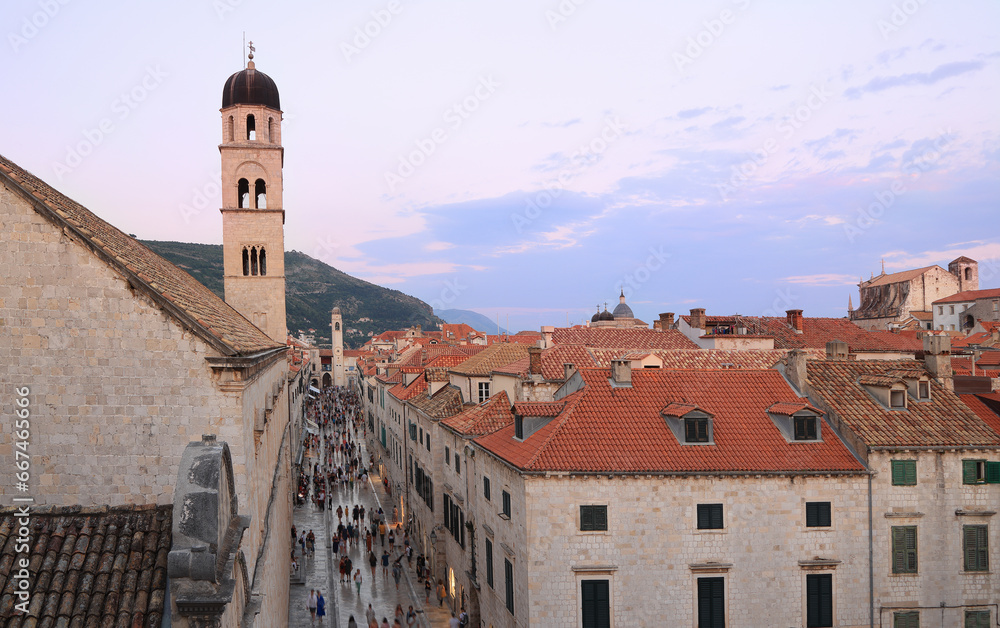 Tourists walking on ancient Stradun street in old city in Dubrovnik at sunset, purple sky background, Croatia