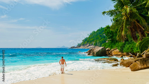 Petite Anse Beach Seychelles, a Young man in swim shorts on a white tropical beach with palm trees Petite Anse beach Mahe Tropical Seychelles Islands. man walking on the beach during a holiday