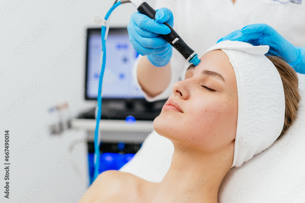 © Vladislav - Close-up shot of a young beautiful woman lying on a couch in a cosmetology center. Young woman doing hydrofacial therapy in beauty spa.