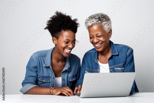 a smiling young woman teaching a senior eldery woman how to use a laptop.