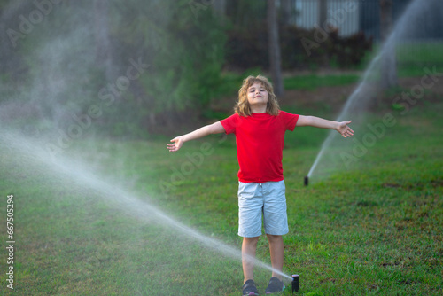 Kid play in garden near irrigation watering sprinkler system. Watering grass with automatic sprinkler. Lawn and gardening concept. Child backyard gardening. Child watering plants, watering sprinkler.