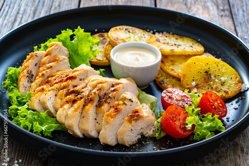 Grilled chicken breast, fried potatoes and fresh vegetables on wooden table

