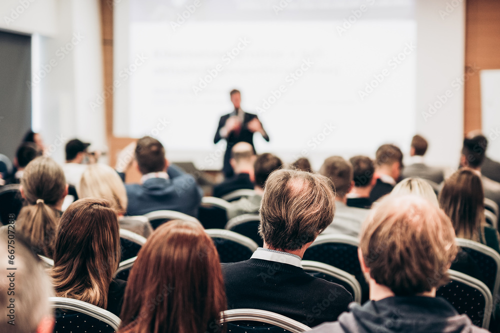 Speaker giving a talk in conference hall at business event. Rear view of unrecognizable people in audience at the conference hall. Business and entrepreneurship concept