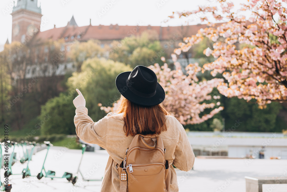 Attractive young female tourist is exploring new city. Redhead 30s girl in black hat resting near Wawel castle, Cracow, Poland. Traveling Europe in spring. High quality photo