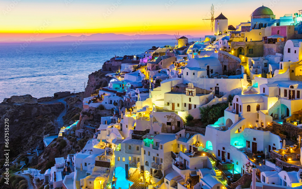 White churches an blue domes by the ocean of Oia Santorini Greece, a traditional Greek village in Santorini at sunset, evening view with lights at the pools of the many hotels of Santorini