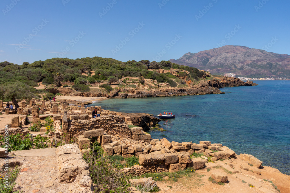 Ruins of the Roman Archeological Park of Tipaza ( Tipasa ), Algeria. The Mediterranean sea and the Mount Chenoua in the background. Boat and people.