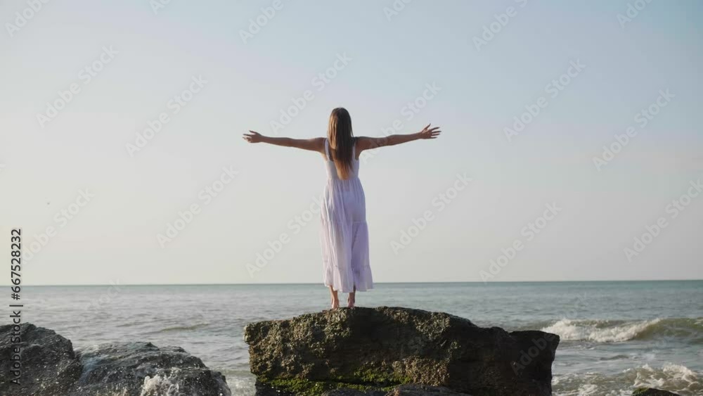 Woman with arms raised standing on rock and enjoying sea at sunrise, back view Woman with arms raised standing on rock and enjoying sea at sunrise, back view