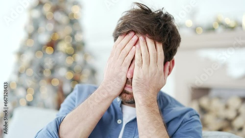 Close up. Man suffering from a hangover sitting on sofa in living room at home during winter New Year Christmas Xmas holidays. Male has a headache, stomachache, feels nauseous after celebrating party photo