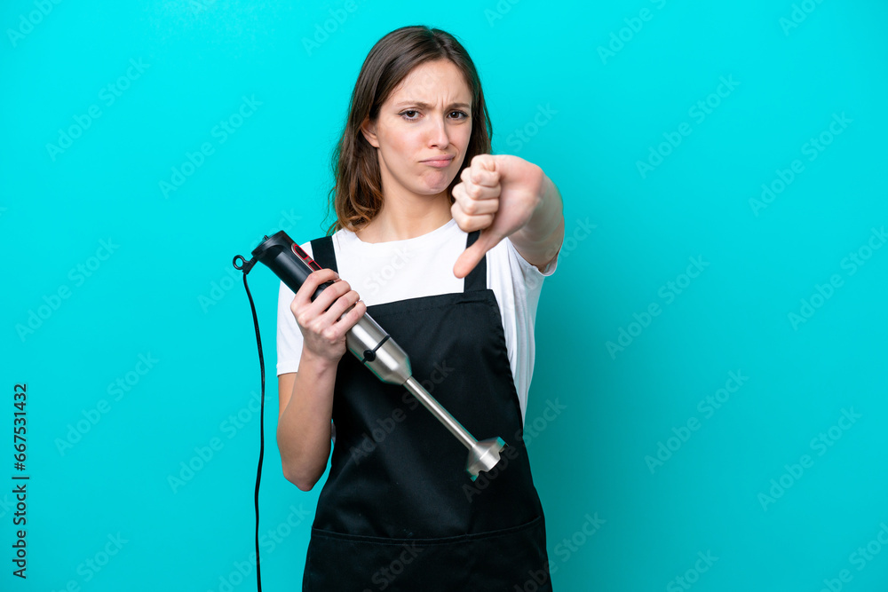 Young caucasian cooker woman using hand blender isolated on blue background showing thumb down with negative expression Young caucasian cooker woman using hand blender isolated on blue background showing thumb down with negative expression