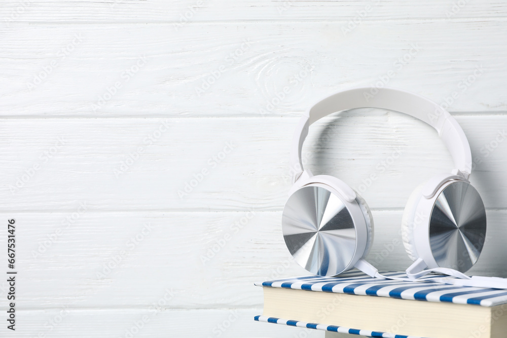 Headphones on book on white wooden background, space for text