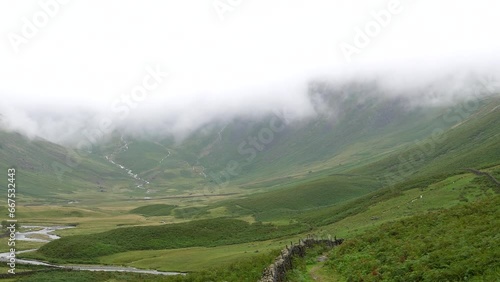 Panning shot of Mosedale Beck stream in the misty mountain valley under low cloud in summer in English Lake District National Park, United Kingdom. photo