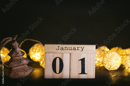 Brown wooden calendar on the black table with garland. Black background. Items to tell date, reminder, planner or meeting. Vintage idea shows 01 January, the beginning of the year. New Year day photo