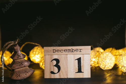 Brown wooden calendar on the black table with New Years garland. Black background. Items to tell date, symbol of appointment, reminder, planner or meeting. Vintage idea shows 31 December, end of year