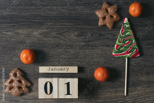 Brown wooden calendar with Christmas tree candy, mandarin, gingerbreads and anis on the dark wooden background. Christmas holidays. Reminder. 01 January, begining of year. Space for text. New Year photo
