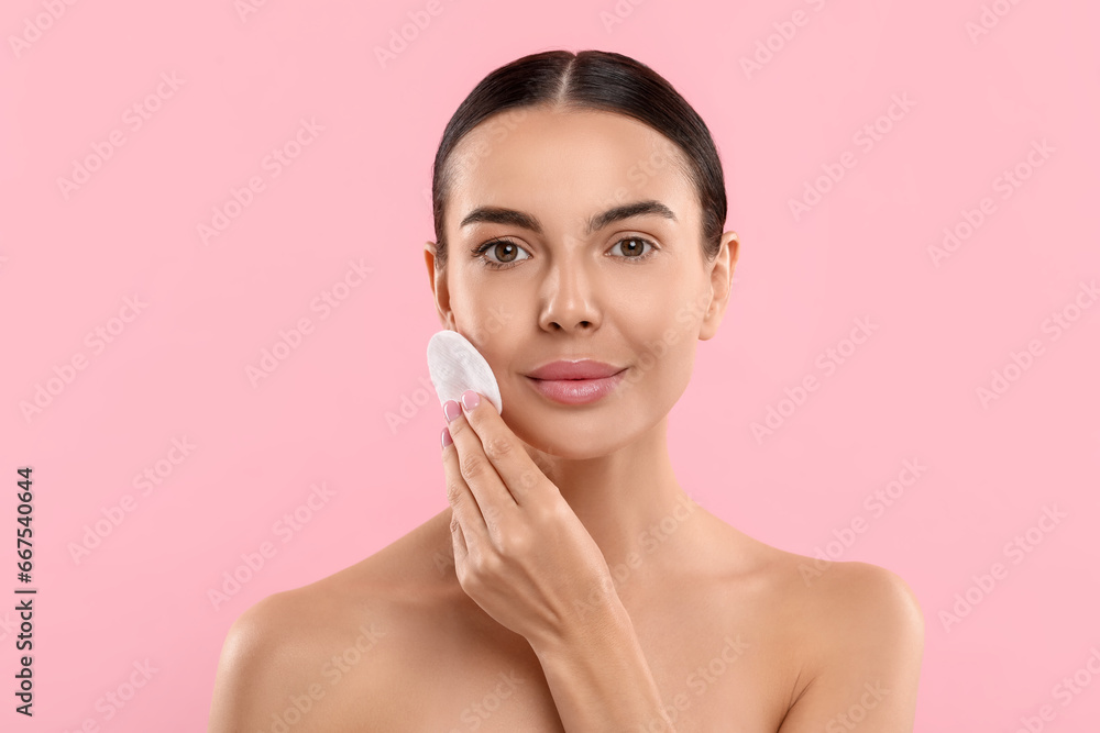 Beautiful woman removing makeup with cotton pad on pink background Beautiful woman removing makeup with cotton pad on pink background