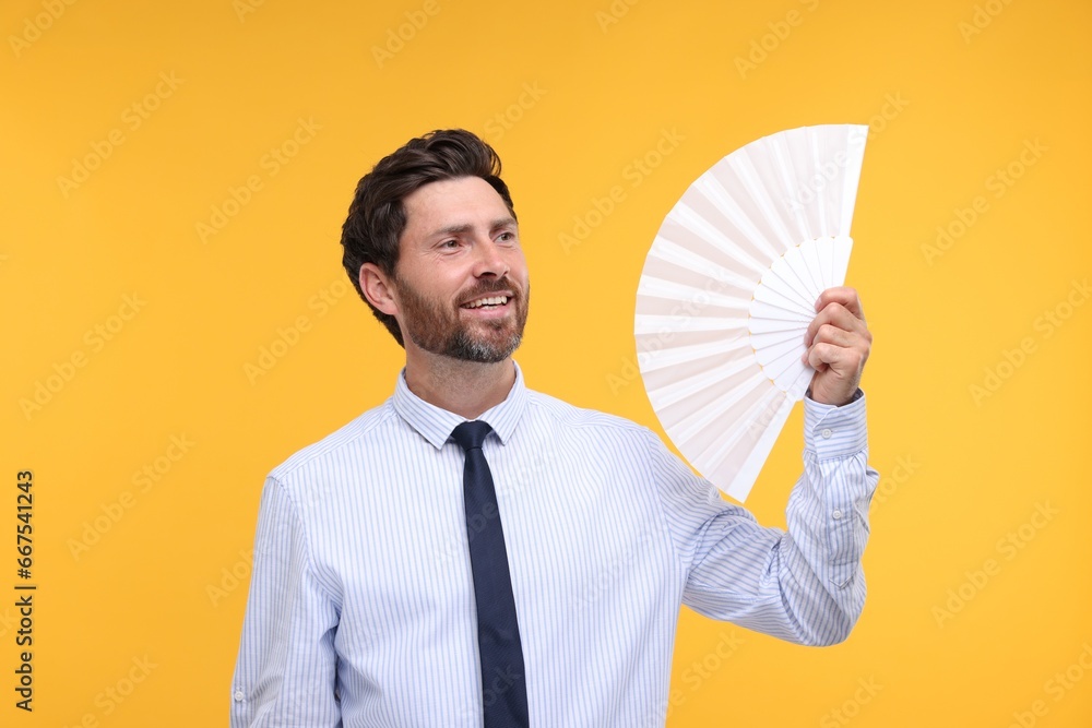 Happy man holding hand fan on orange background Happy man holding hand fan on orange background