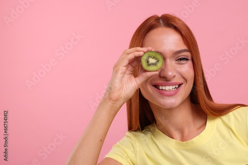 Happy woman covering eye with half of fresh kiwi on pink background, space for text