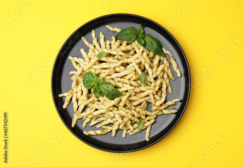 Plate of delicious trofie pasta with pesto sauce and basil leaves on yellow background, top view photo