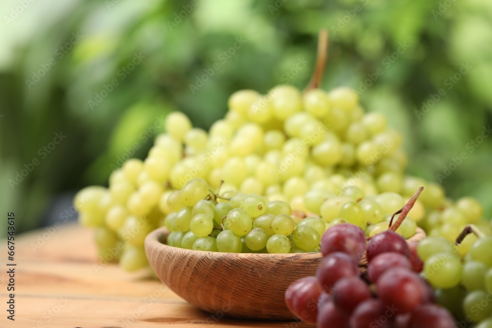 Different fresh ripe grapes on wooden table against blurred background, space for text