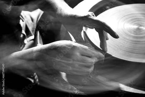 Black and white image of the hands of a young female potter throwing plates on a spinning wheel. Blurring to show motion.